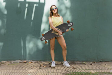 adolescente vestida com camiseta básica amarela, tênis branco e bermuda jeans, segurando um skate