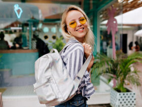 Mulher com look despojado de calça jeans, mochila, camisa listrada e óculos de sol