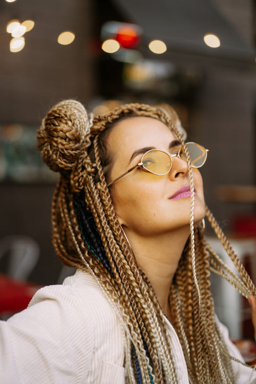 jovem mulher com tranças estilo hippie e óculos curtindo sua própria vibe