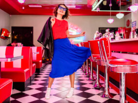 Mulher usando um look dos anos 60 com blusa vermelha vestido azul e óculos escuro