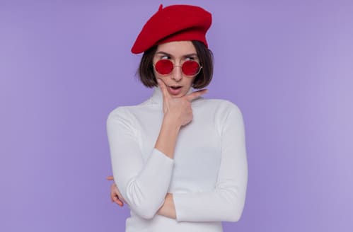 joven mulher usando um blusa branca, óculos com lente avermelhada e uma boina pillbox vermelha