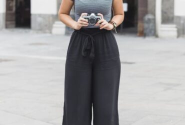 Mulher com camera na mão usando uma calça pantalona