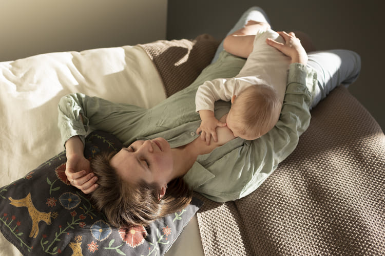 mulher deitada provavelmente sonhando e amamentadno seu bebe ao mesmo tempo