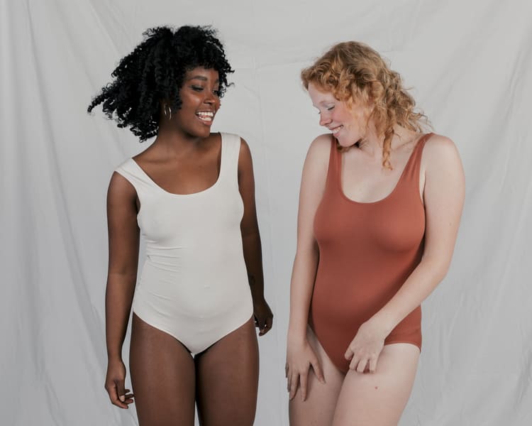 Duas mulheres usando bodies plus size, sendo uma cor nude e outra na marrom.