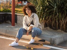 Mulher sentada na guia usando um look com calça joguer jeans e um tênis allstar branco