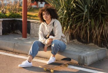 Mulher sentada na guia usando um look com calça joguer jeans e um tênis allstar branco