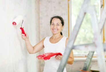Mulher com pincel na mão pintando uma parede de sua casa
