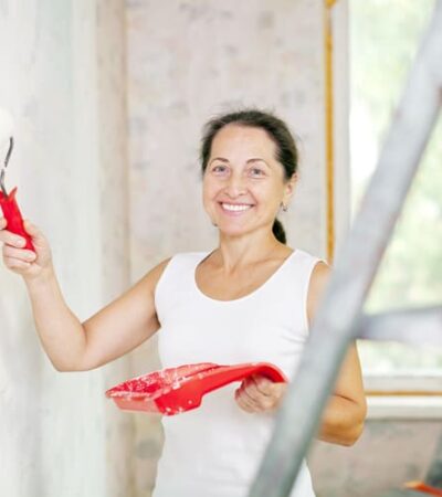 Mulher com pincel na mão pintando uma parede de sua casa