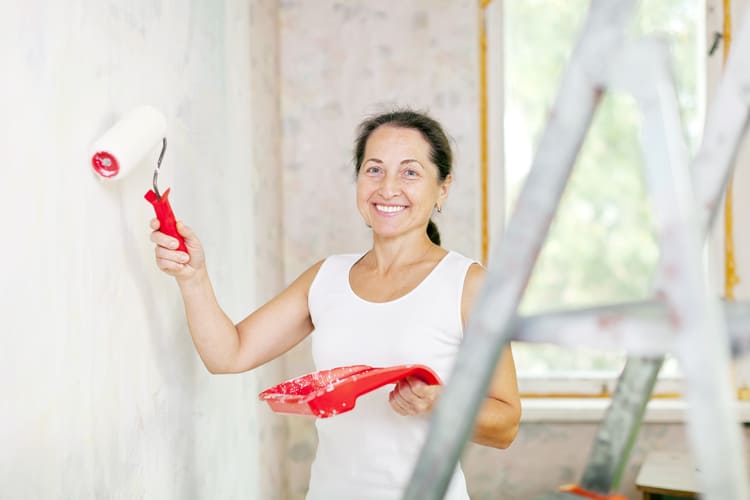 Mulher com pincel na mão pintando uma parede de sua casa